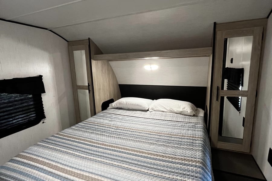 Modern RV rental bedroom with a comfortable queen bed, built-in storage, and bright overhead lighting.