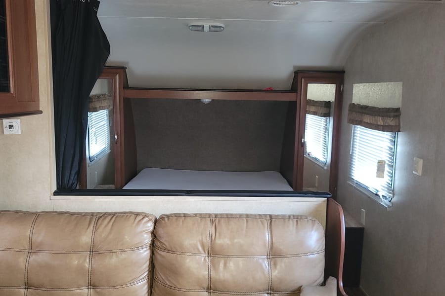 Bright RV rental interior featuring a large, tufted light brown leather sofa, windows, and wood cabinetry.