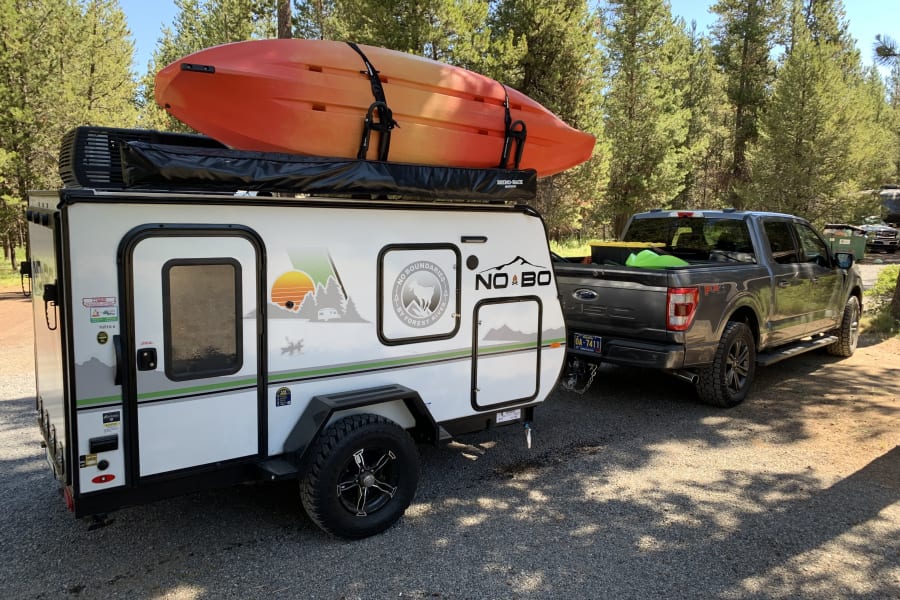 RV rental adventure: A No Boundaries travel trailer with a kayak is hitched to a Ford F-150, ready for outdoor fun.