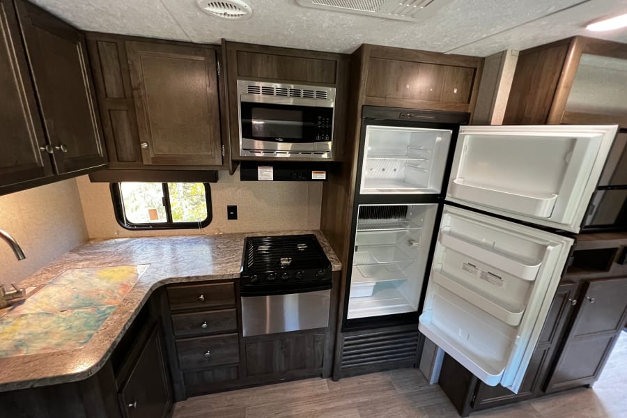 Inside an RV rental: a modern kitchen with open refrigerator, microwave, gas stove, dark cabinets, and ample counter space.