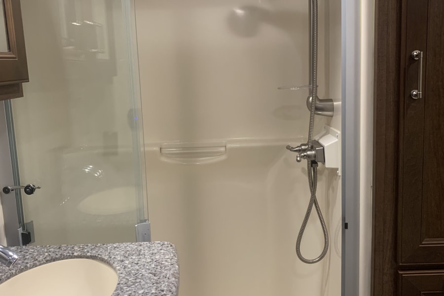 Modern RV rental bathroom: a spacious shower with glass door and handheld shower, plus a stylish sink with granite counter.