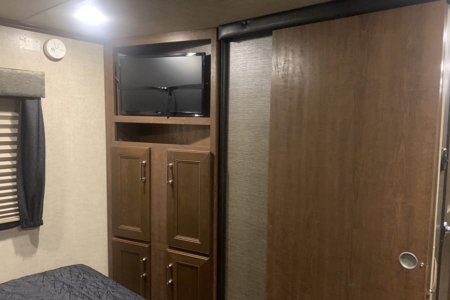 RV rental interior: Bedroom with built-in storage, TV, and a wooden sliding door for efficient space.