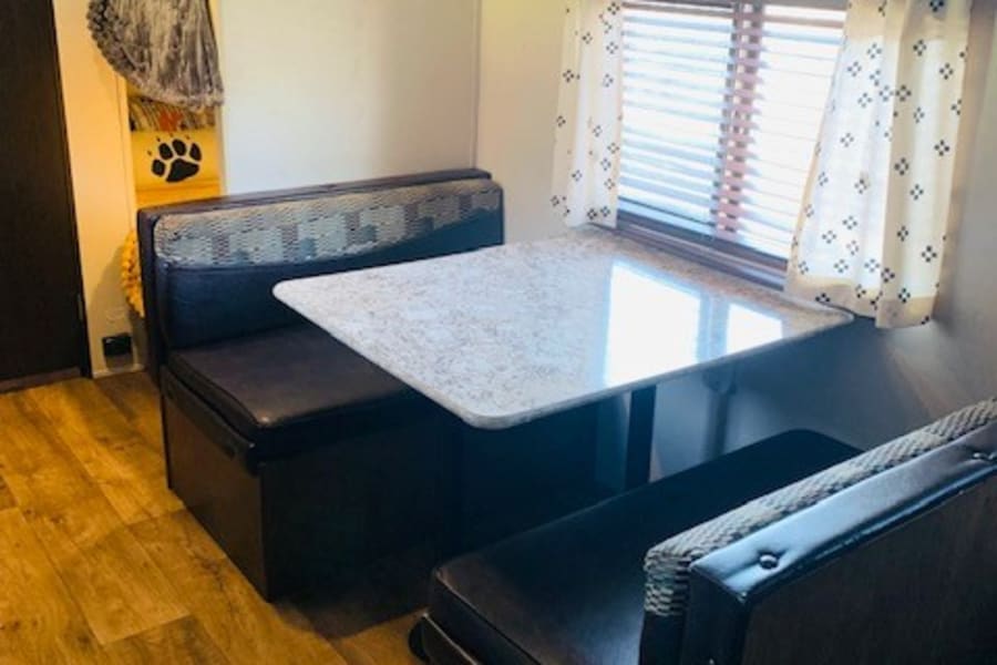 Cozy dinette in an RV rental, featuring table, benches, overhead cabinets, AC unit, and wood-look floor.