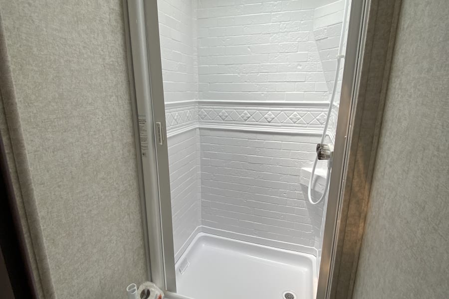 Inside an RV rental bathroom: a clean, white shower stall with a handheld showerhead & a compact toilet.