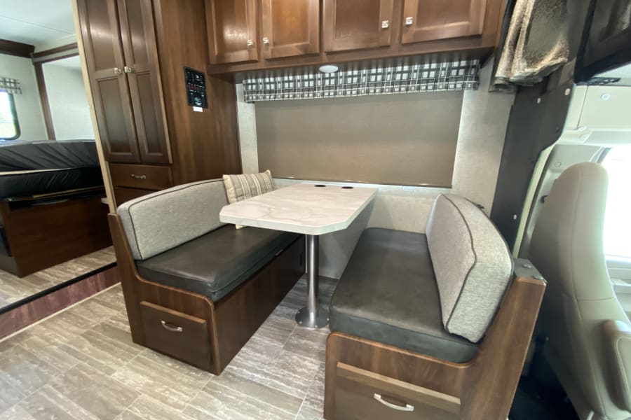 RV rental interior: Features a dinette with padded benches, a central table, overhead storage, and a glimpse of the bed.