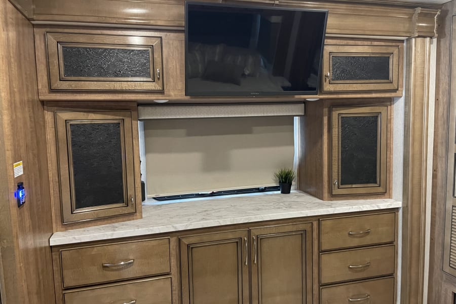 Modern RV rental bedroom setup with built-in wooden cabinets, flat-screen TV, and countertop. A cozy, functional interior.