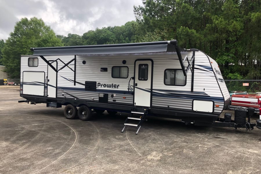This Prowler travel trailer, ideal for an RV rental, is shown with its awning extended and steps down, parked on asphalt.