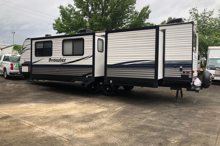 A large Prowler travel trailer RV rental with extended slide-outs, parked on a concrete lot.