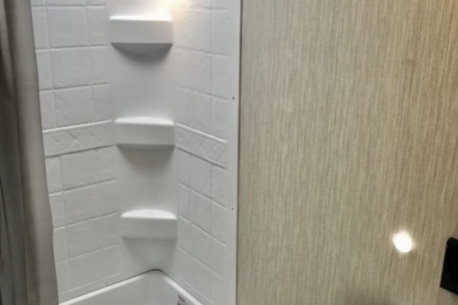 RV rental bathroom features a bright, compact shower-tub combo, built-in shelves, and a partial sink view.