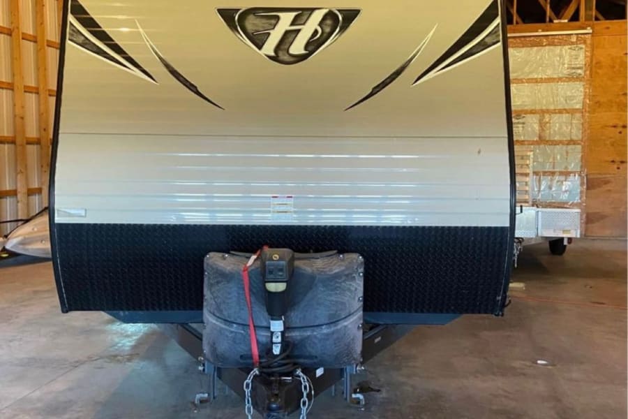 Front view of an RV rental: a light-colored Hideout travel trailer with black lower panel, parked indoors.