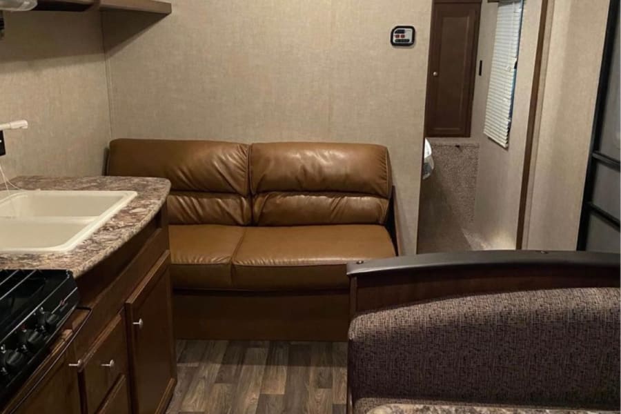RV rental interior: a compact living space with a kitchen, brown sofa, and dinette, featuring wood-look flooring.