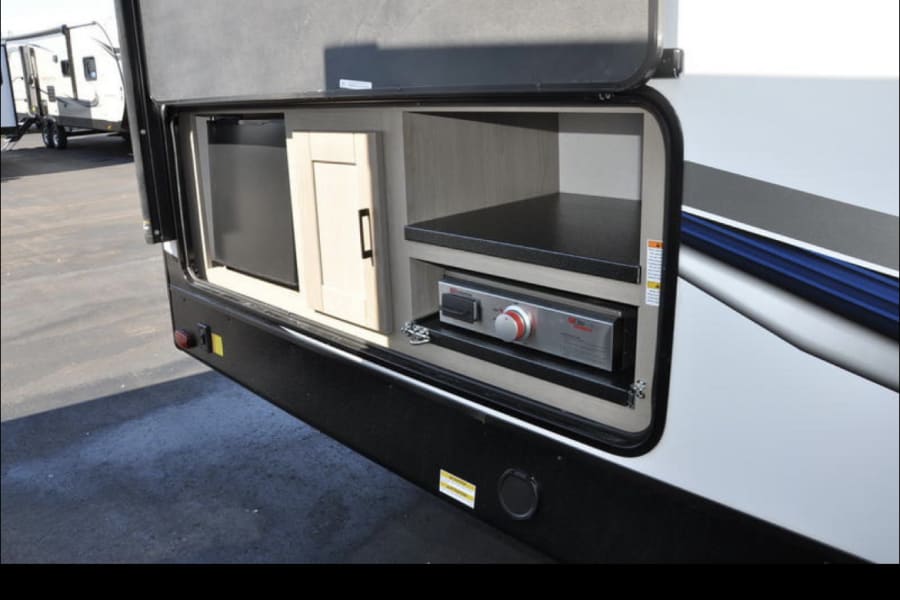 RV rental: Outdoor kitchen with mini-fridge, cabinet, and built-in grill/stove. Ideal for outdoor cooking & storage.
