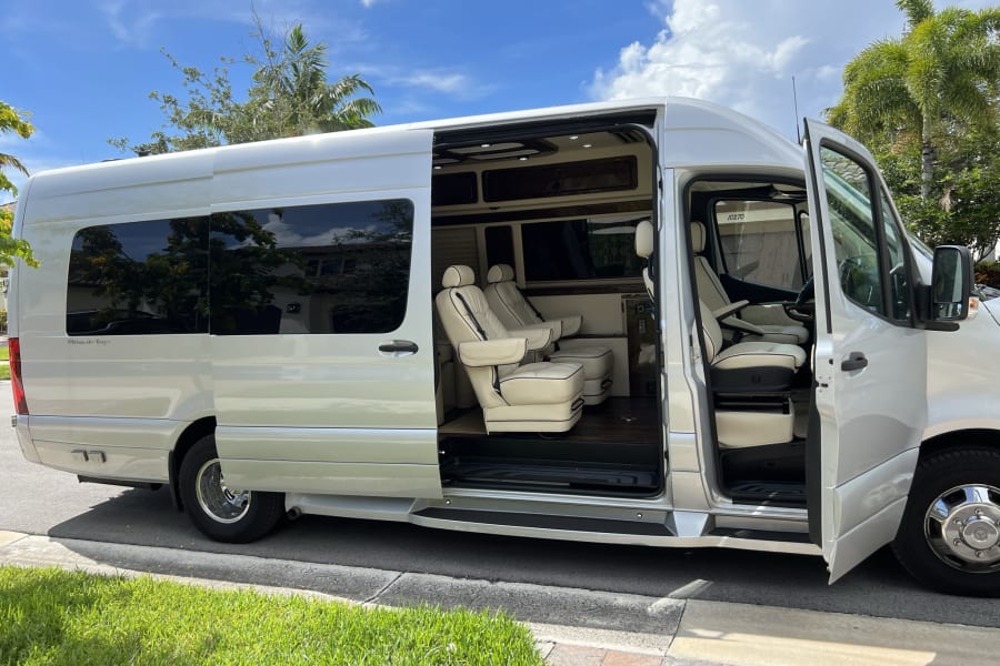 Luxury silver Mercedes Sprinter RV rental van. Open side door reveals a spacious, plush cream interior for travel.