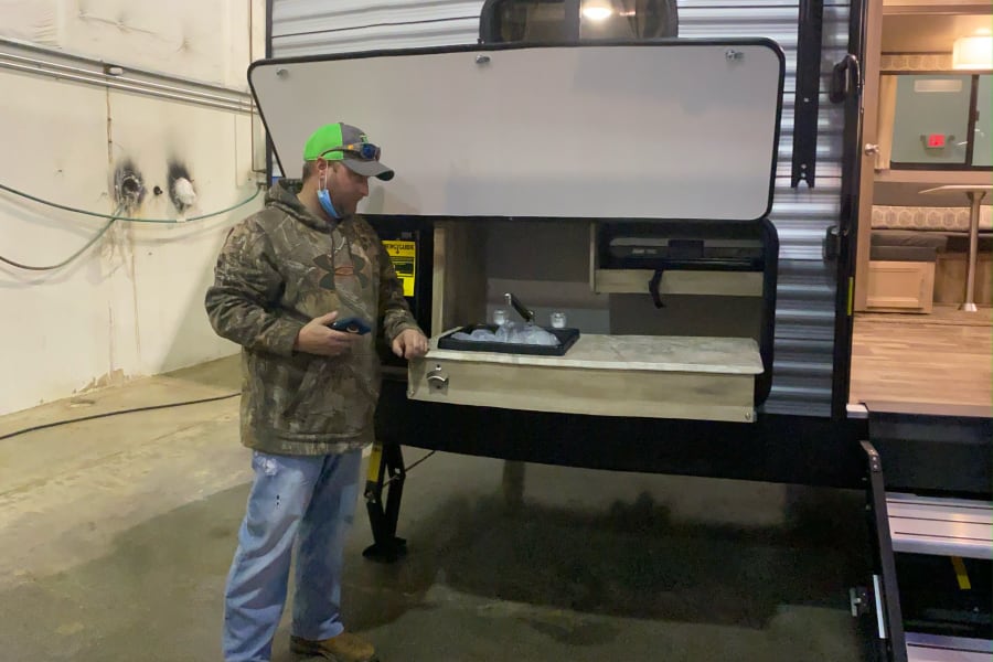 A man in a cap examines an RV rental with its convenient outdoor kitchen, featuring a sink and prep area.