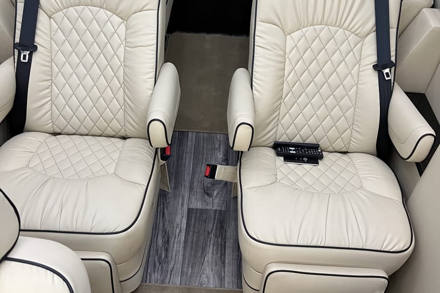 Inside a luxury RV rental, featuring two comfortable cream leather captain's chairs with diamond-quilted upholstery.