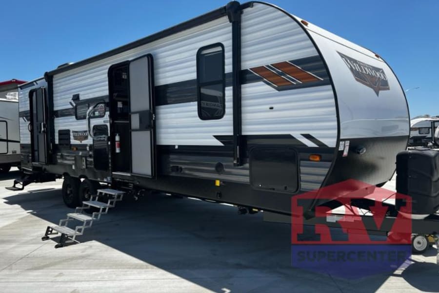 Modern Wildwood travel trailer RV, perfect for rv rental trips. Features white/grey exterior, extended steps, on a sunny day.