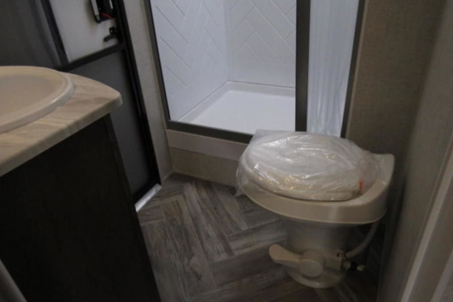 Compact RV rental bathroom: Features a sink, shower, and a new, protected toilet.