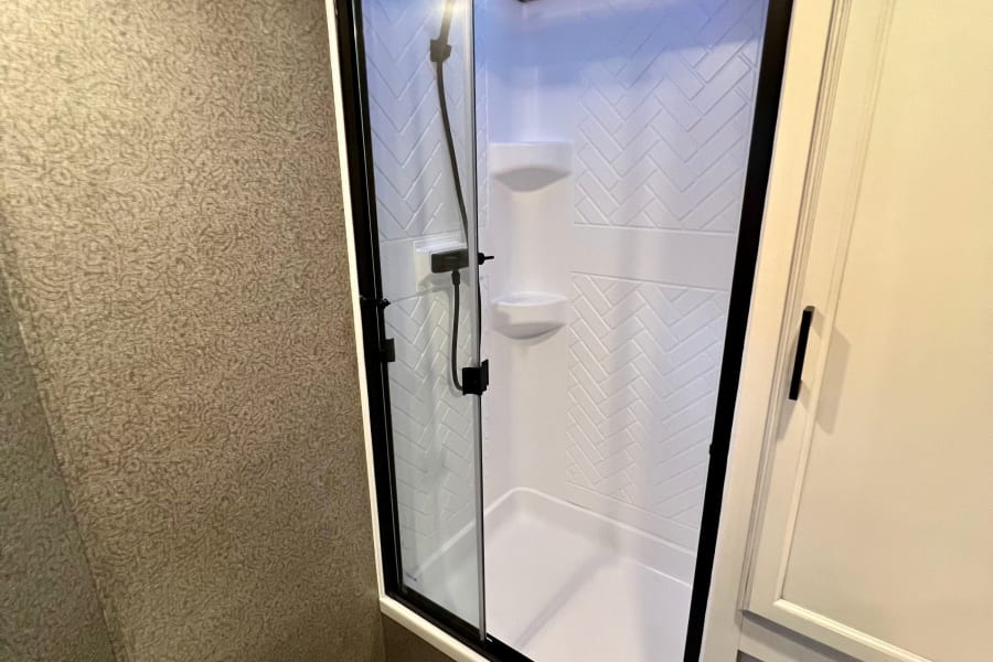 This RV rental's efficient bathroom includes a white toilet and a contemporary glass shower stall with blue accent lighting.