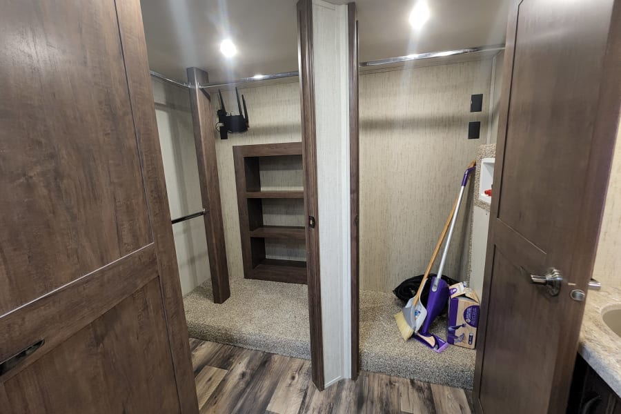 RV rental: multi-purpose closet/storage with wood-look doors, shelves, built-in router, and cleaning supplies on carpet.