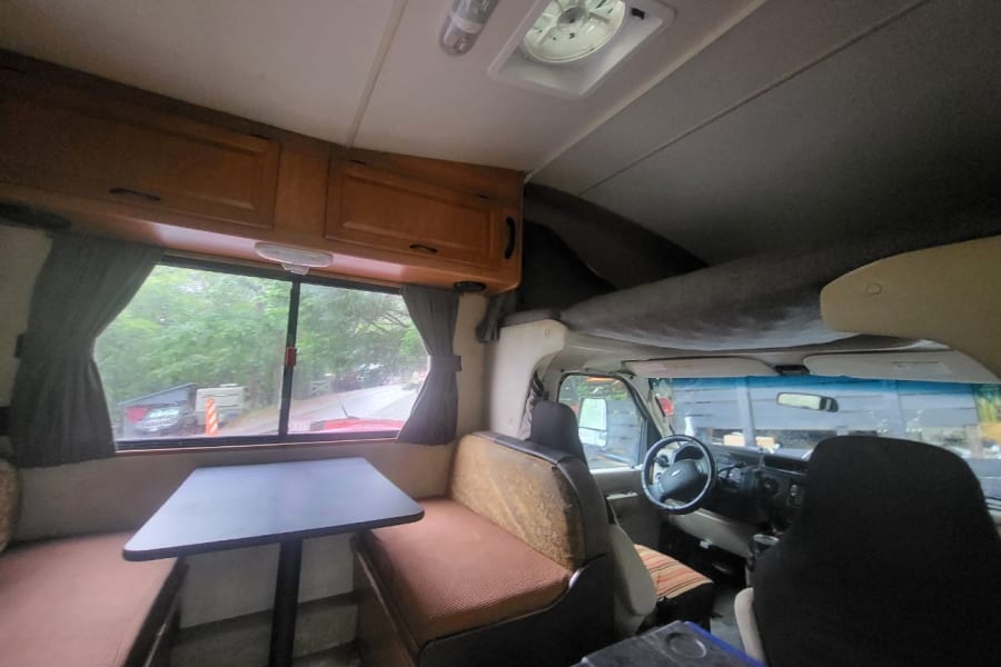 Interior view of an rv rental showing a dinette, overhead bunk, and the front driving area, ideal for travel.