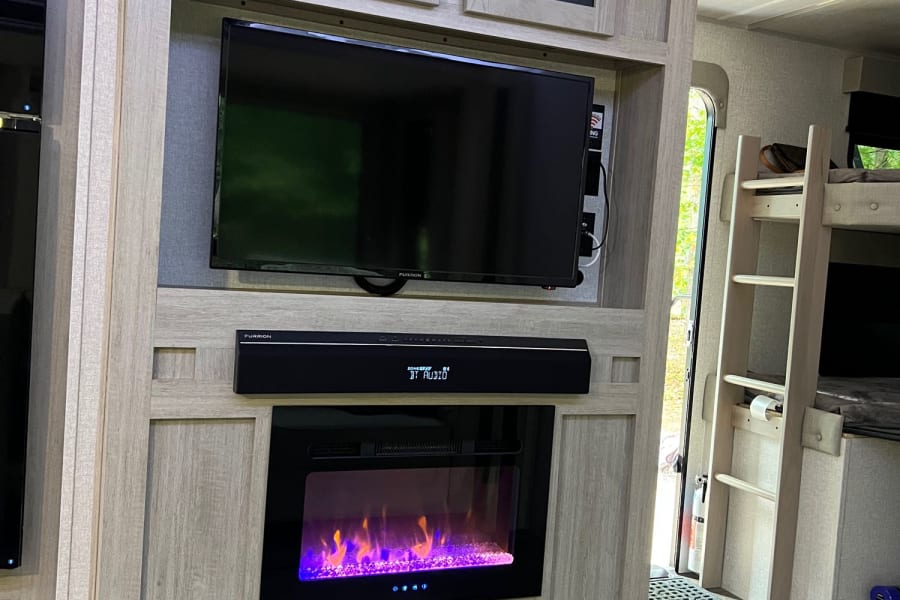 Modern RV rental interior featuring an entertainment center with TV, electric fireplace, and bunk beds.