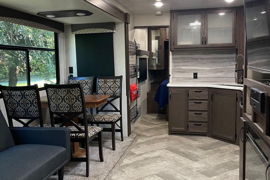 Modern RV rental interior: cozy living, dining with patterned chairs, & sleek kitchen. Bright for travel.