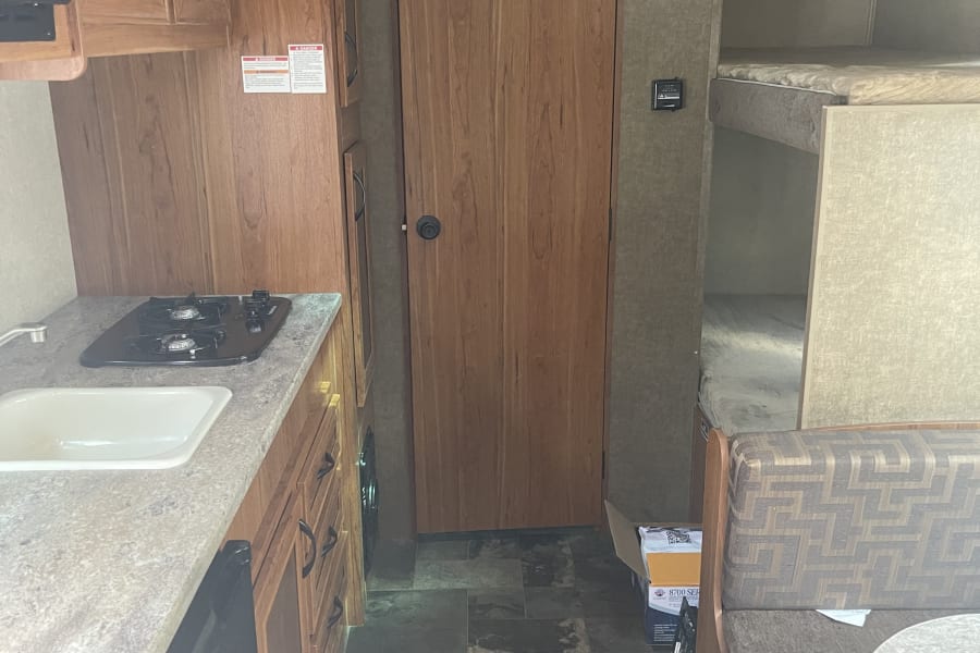This RV rental interior showcases a compact kitchen, central door, and comfortable bunk beds for travel.