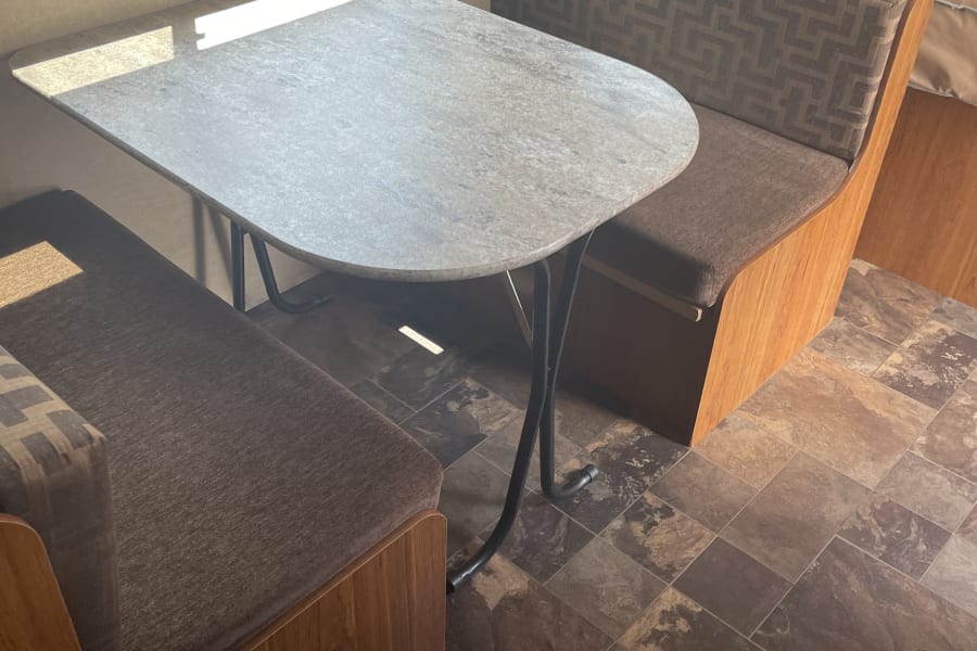 RV rental's inviting dinette with a light grey table, patterned brown bench seating, and tiled floor for comfy travel.