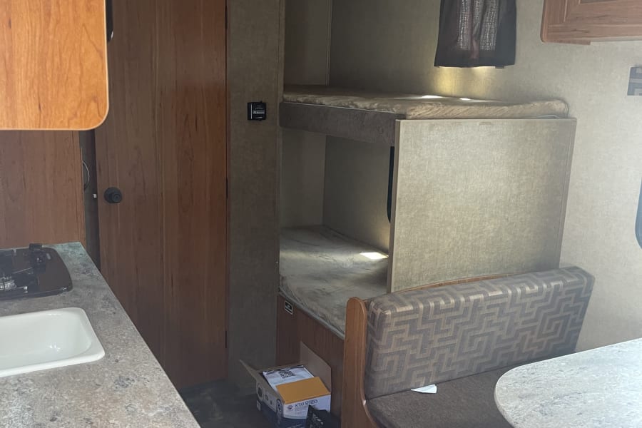 Spacious RV rental interior featuring bunk beds, a dinette, and a compact kitchen with a sink and stovetop.
