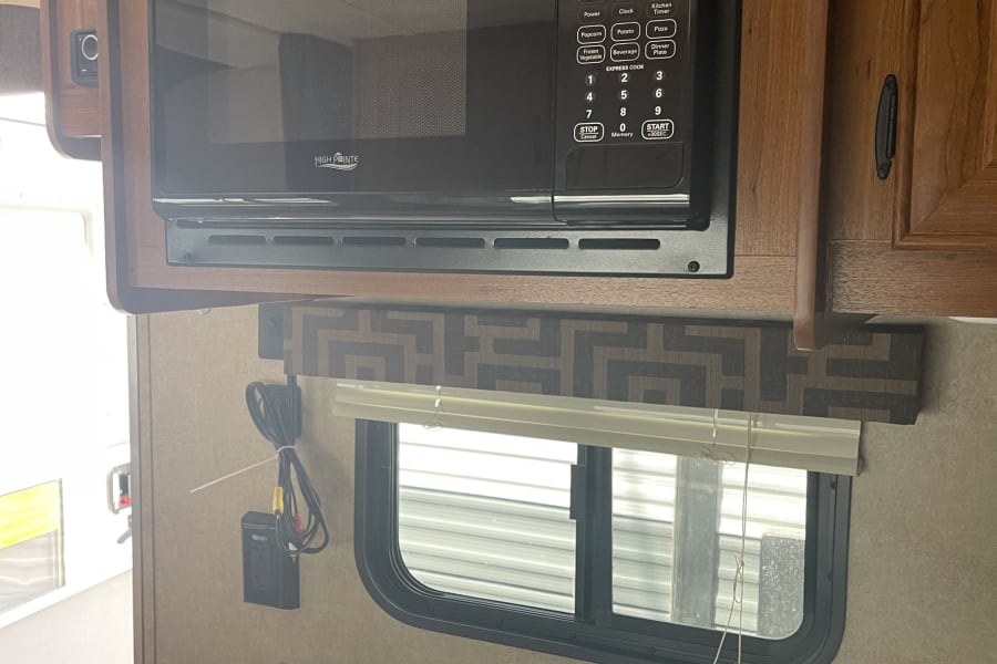 RV rental kitchenette with a built-in High Pointe microwave, speckled countertop, sink, and window.