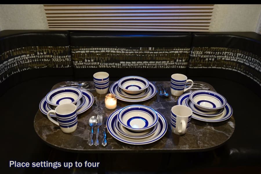 Cozy RV rental dining area with complete place settings for four, featuring blue-striped dinnerware. Perfect for meals on the go.