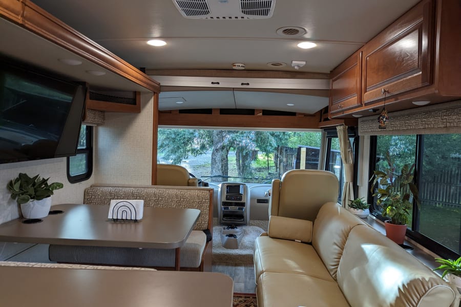 This RV rental's inviting interior showcases a dining booth, sofa, and driver's area, perfect for travel comfort.