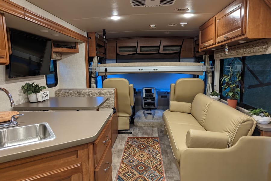 Bright rv rental interior featuring a full kitchen, dining booth, sofa, and front cabin with an overhead bed.