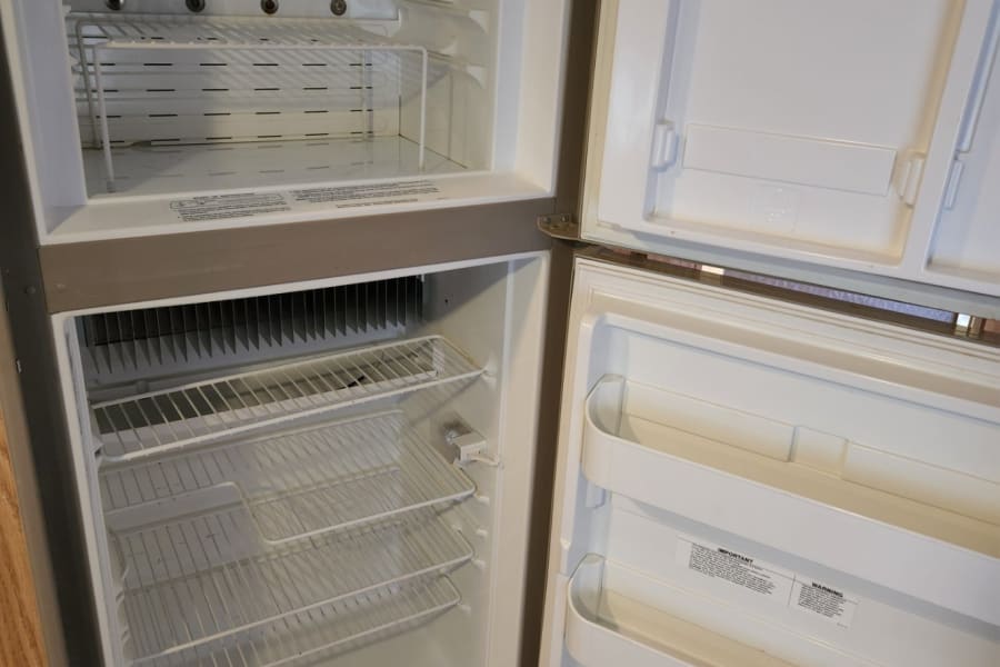 Clean, empty RV rental refrigerator/freezer with open doors, shelves visible, ready for use.