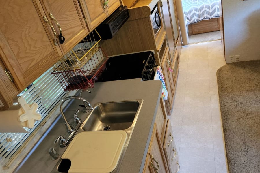 Spacious RV rental interior with full kitchen, sink, stove, fridge, and cozy bedroom. Perfect for travel adventures.