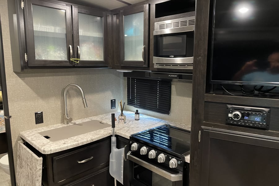 RV rental: modern kitchen with dark wood cabinets, sink, microwave, oven, TV, and stereo. Compact & functional space.