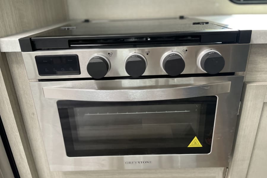 Stainless steel Greystone RV stove & oven, seen in an RV rental kitchen. Features a 4-burner cooktop and digital display.