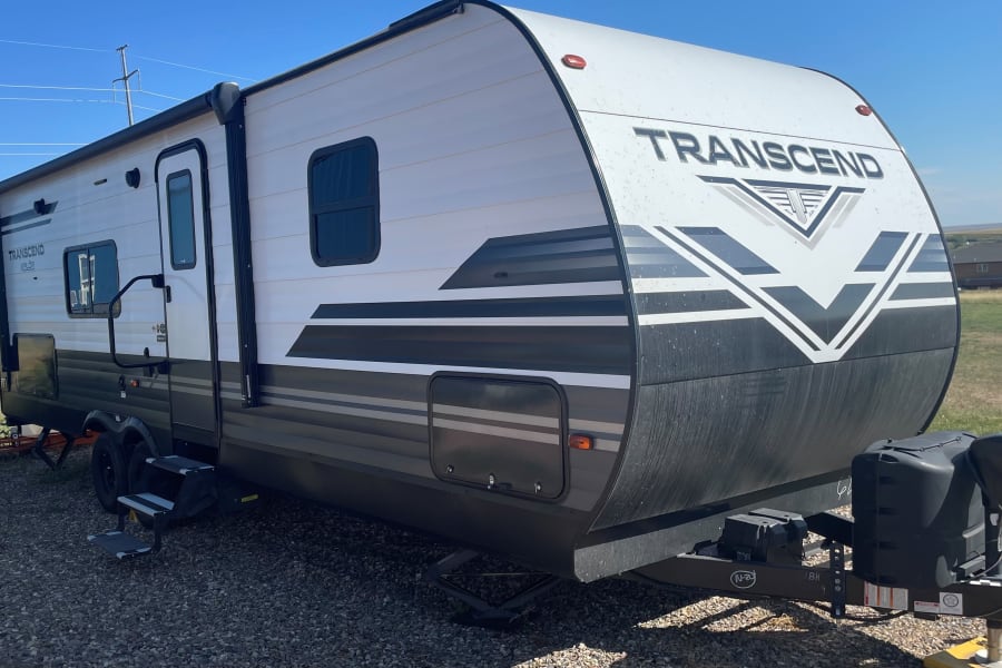 Ready for your next rv rental adventure: a pristine Transcend travel trailer parked in an open field under a blue sky.