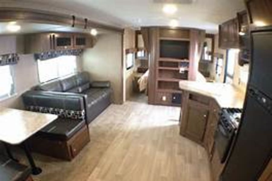 This bright, spacious RV rental interior shows a living area with sofa and dinette, kitchen, and glimpse of the bedroom.
