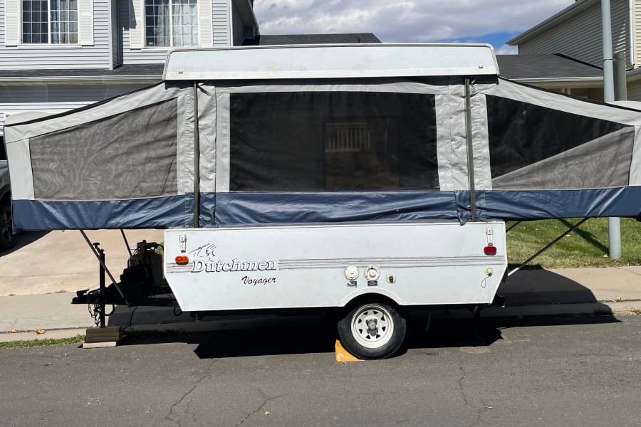 An expanded white Dutchmen Voyager pop-up camper is parked on asphalt, ready for an rv rental adventure.