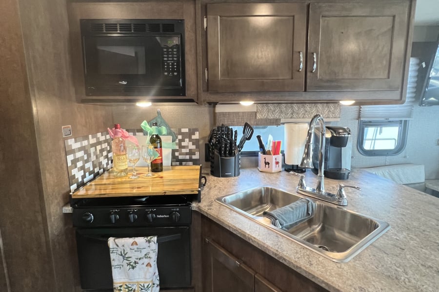 Modern RV rental kitchen features a microwave, stove, sink, and ample counter space, ready for your next adventure.
