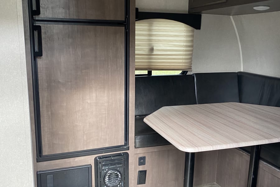 RV rental interior featuring a Dometic fridge, dinette with table and L-shaped seating, cabinets, and a window.