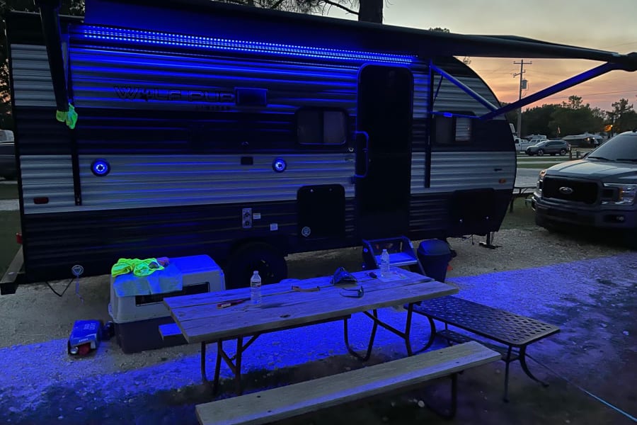 Enjoying the night at an RV rental site! Blue LED lights highlight the camper and picnic area at dusk.