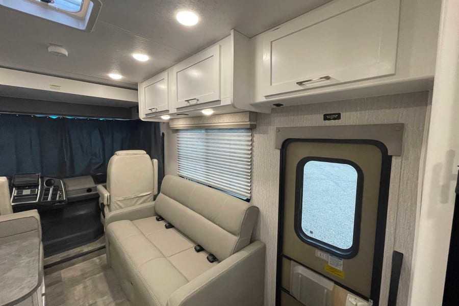 Bright motorhome rv rental interior with beige sofa, driver's area, ample storage cabinets, and side entrance.
