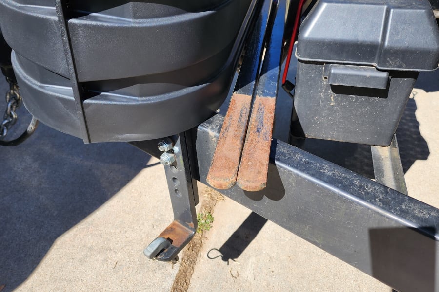 RV rental trailer hitch setup: battery box, propane tank, and rusty weight distribution bars on concrete.