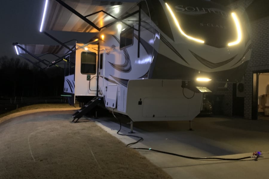 A modern rv rental glows at night, showcasing bright LED awning lights and distinctive front accents.