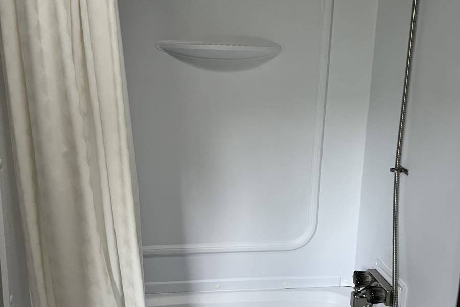 Compact white shower/tub combo in an RV rental, featuring a curtain and handheld shower.