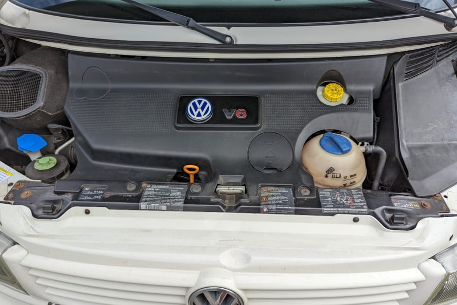 Volkswagen V6 engine bay of an RV rental, showing coolant, oil, and brake fluid reservoirs for maintenance.
