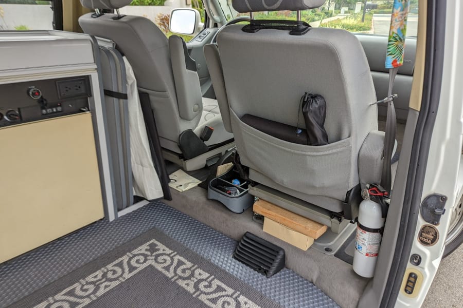 RV rental camper van interior showing rear seats, kitchenette, floor, and a mounted fire extinguisher for safety.