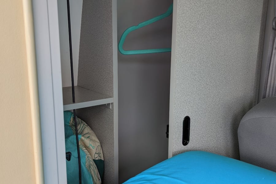 RV rental: Compact interior wardrobe with a turquoise hanger, lower shelf, and a vibrant blue bed.